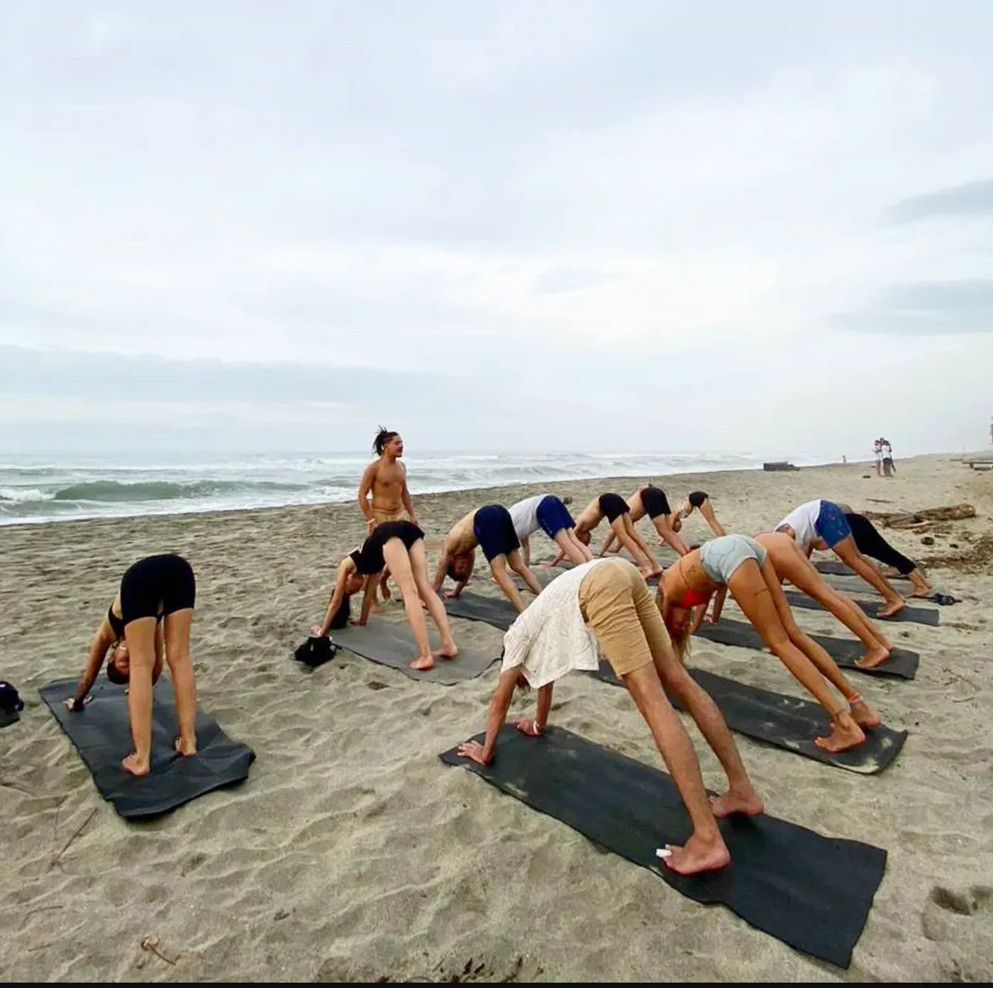 A group practicing yoga on the beach, guided by their teacher