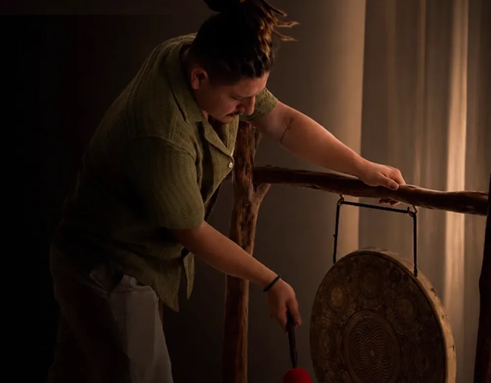 A sound therapist playing a gong in a softly lit room